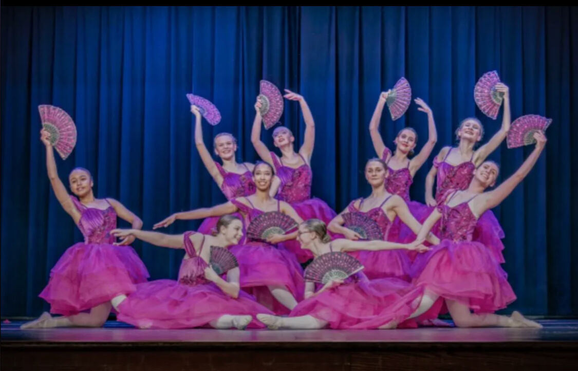 Reverence Studios dancers in magenta dresses posing with lace fans on a recital stage
